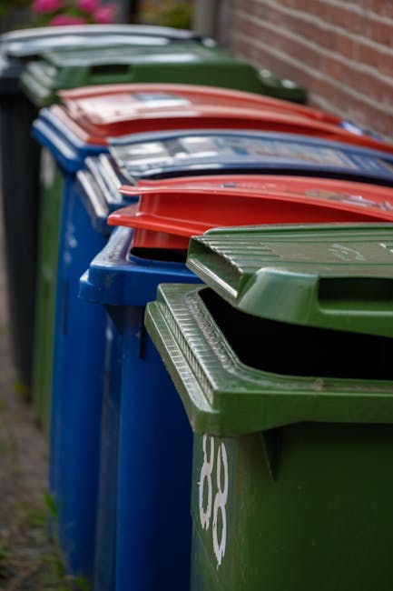 A crumpled orange plastic rubbish bag lying on a paved surface near the edge of a concrete curb and a parked vehicle's wheel in a street setting. The bag appears to be made of thin, flexible plastic w